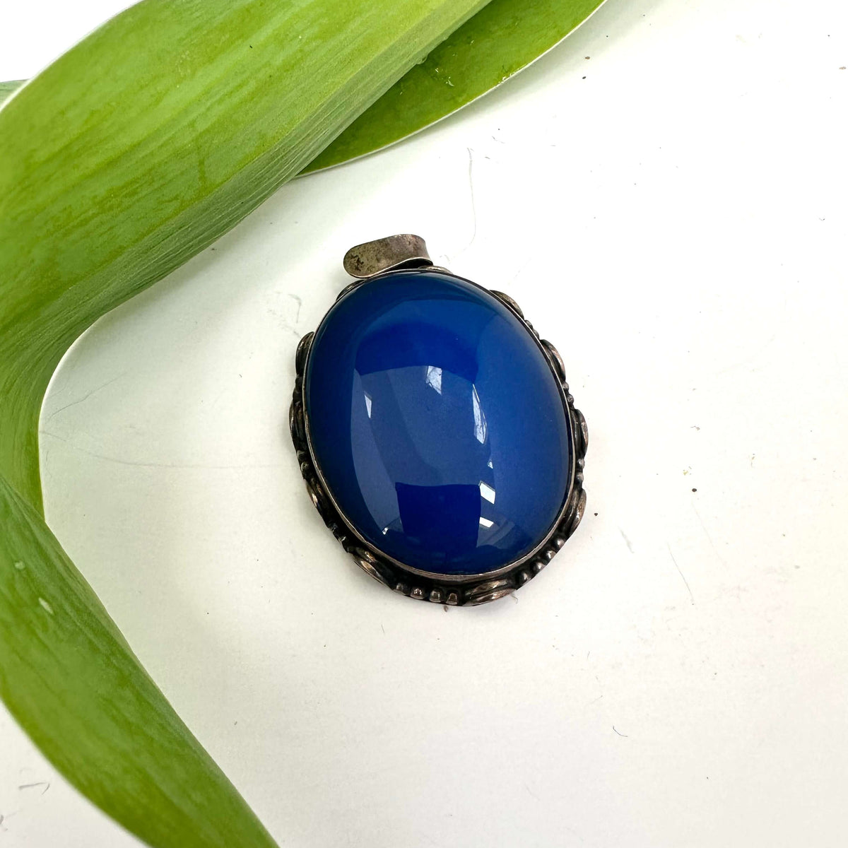 Vintage blue agate pendant in oxidized sterling silver with a deep cobalt-blue hue resting on a green leaf.