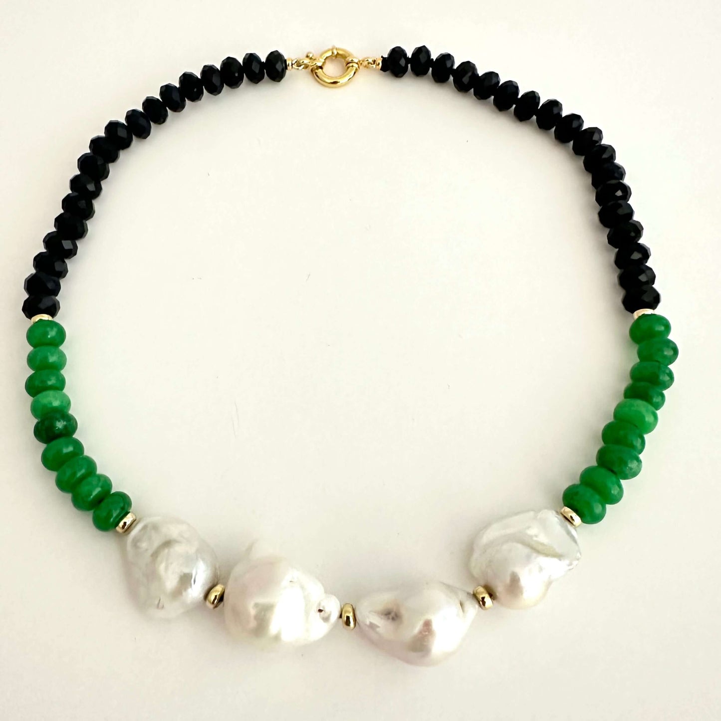 A beaded necklace featuring black faceted beads on one side, vibrant green beads on the other, and 4 large white baroque pearls in the center, separated by small gold spacers and connected by gold chain links.