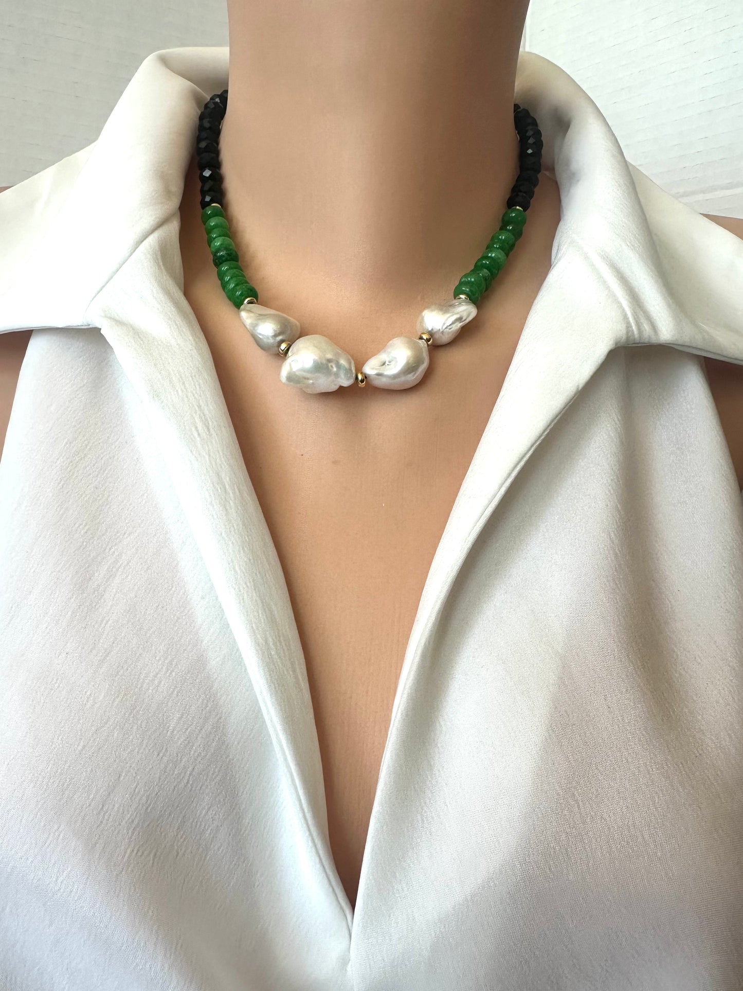 A close-up of a necklace worn on a mannequin or model torso, featuring 4 large irregular white baroque pearls in the center, flanked by green beads and black beads, styled with a white collared shirt.