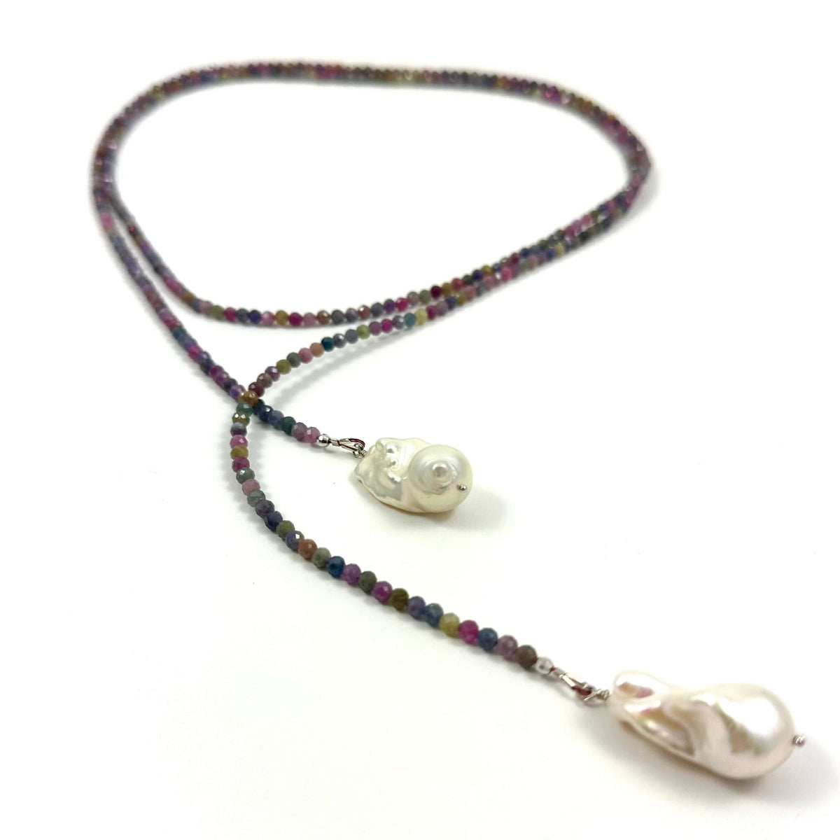 A beaded necklace with iridescent multicolor beads, featuring a carved white bead pendant and a larger teardrop-shaped white pearl pendant, displayed on a clean white background.