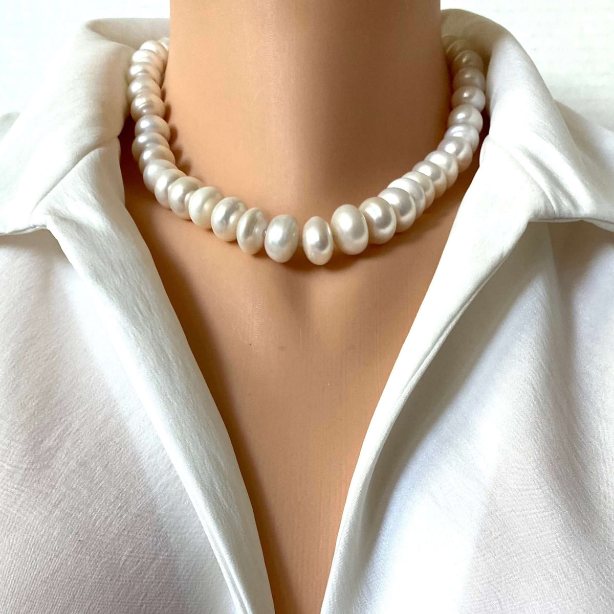 A close-up of a white pearl collar necklace worn on a mannequin or model torso, paired with a white satin blouse.