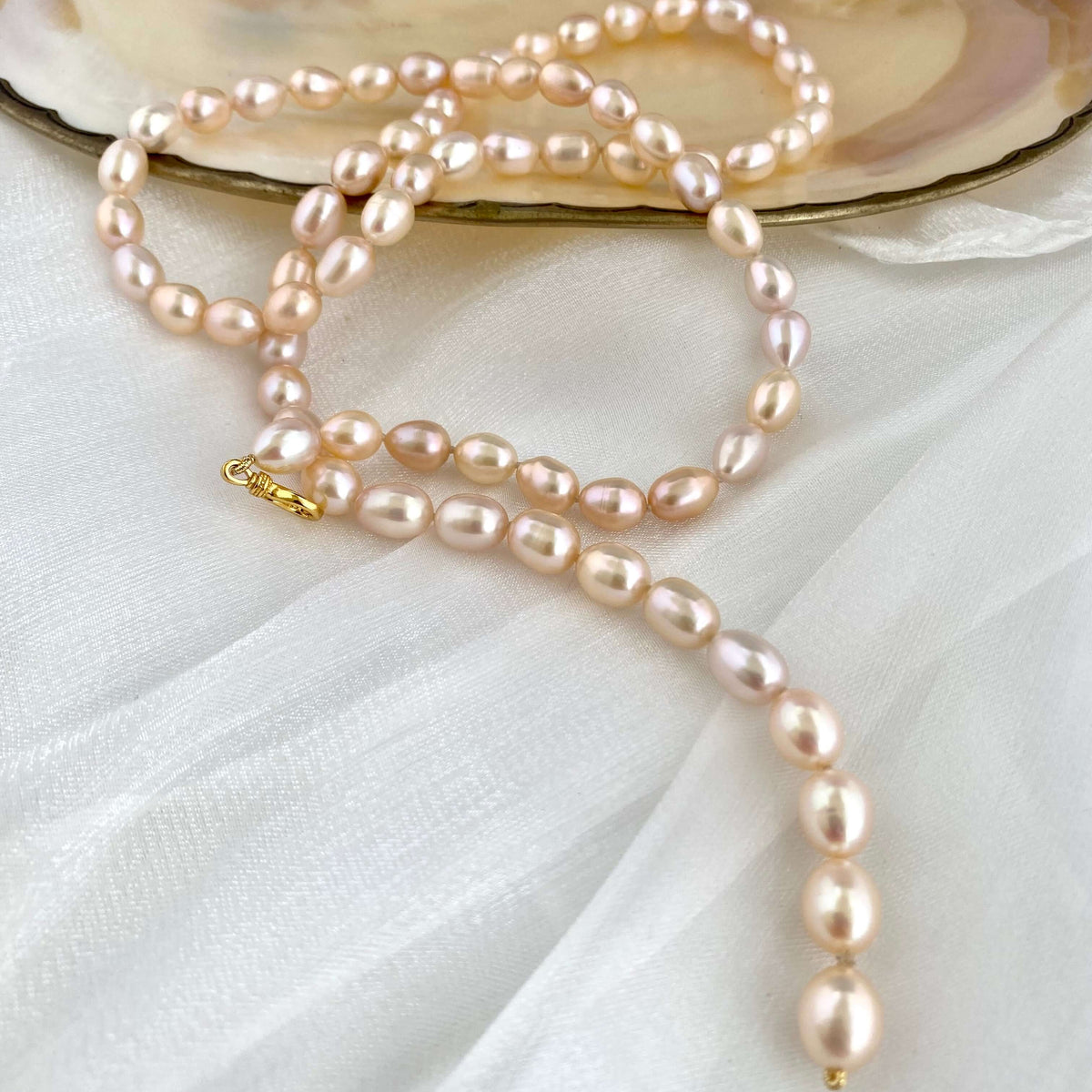 Pearl necklace draped over an open shell on a white fabric background