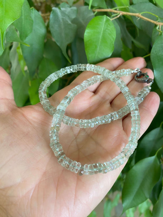 Green amethyst beaded necklace with diamond & emerald pavé clasp held in hand against green foliage.