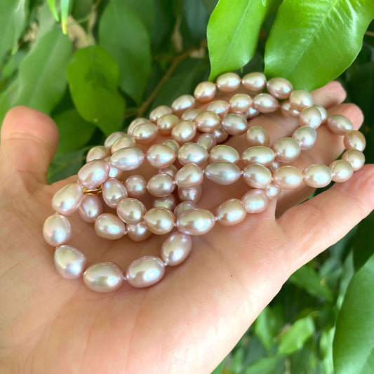 Pearl necklace held in a hand with green leaves in the background