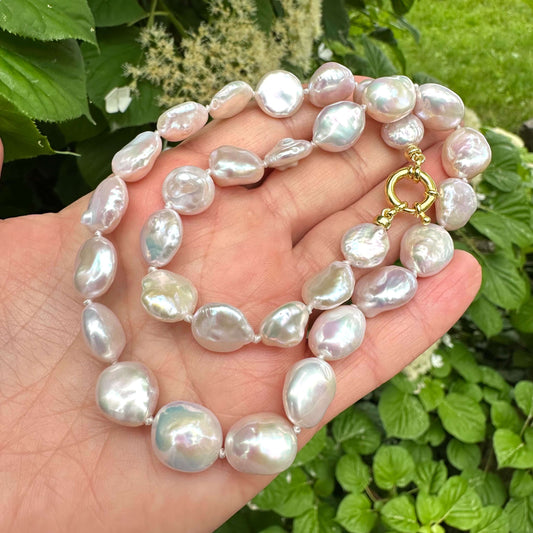 Close-up of coin pearl necklace held in hand against summer foliage