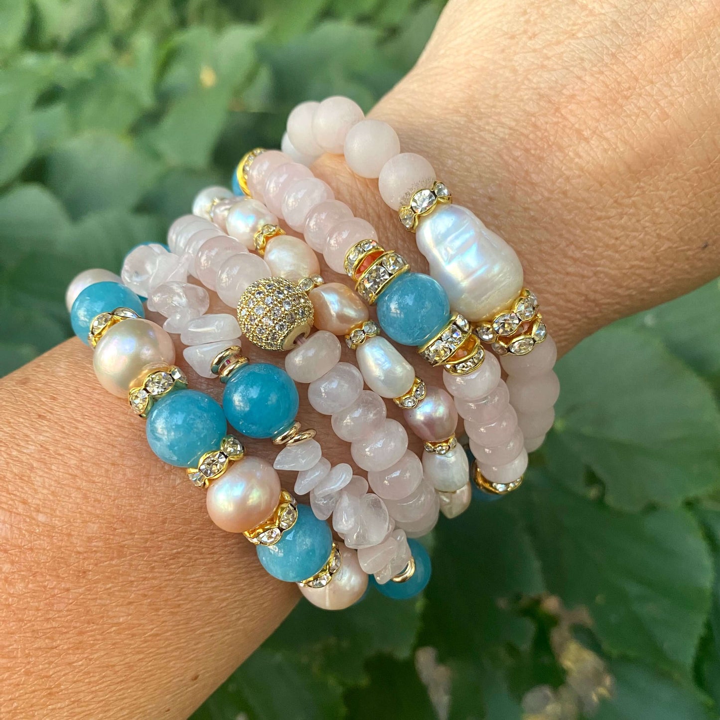 Rose quartz stretch bracelet with gold accent beads, featuring pearls and turquoise stones, stacked stylishly on a wrist.