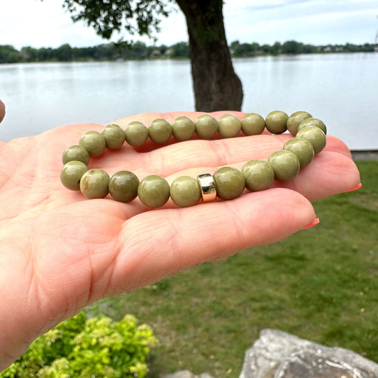 Olive Green Jasper Bracelet – 6mm or 8mm, 14K Gold Filled held in hand by a lakeside.