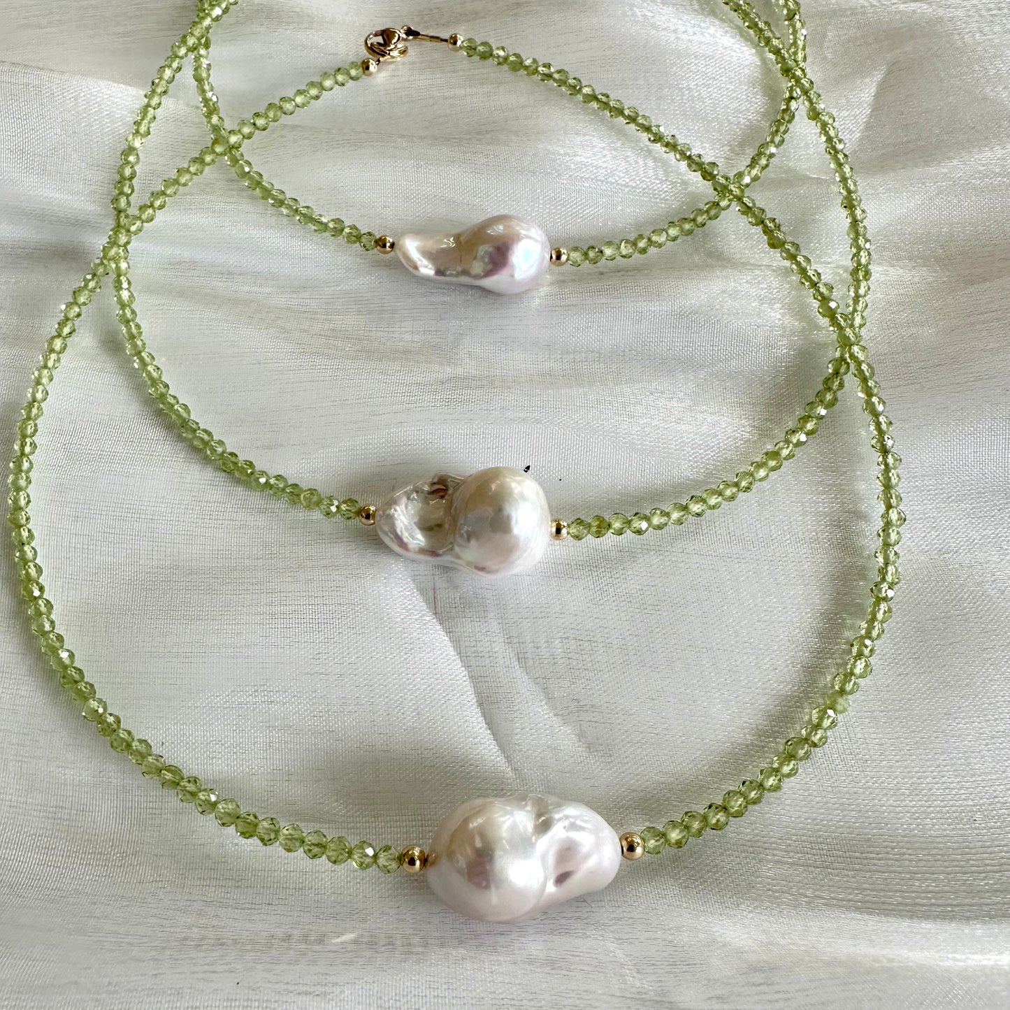 Three peridot and baroque pearl necklaces stacked on white cloth