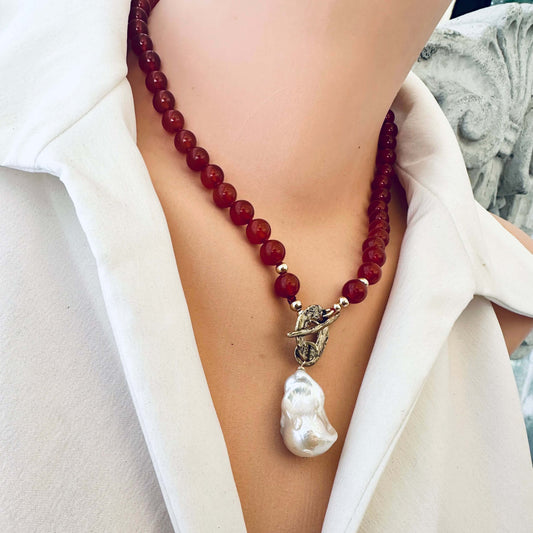 Red agate toggle necklace with baroque pearl pendant displayed on mannequin, frontal close-up