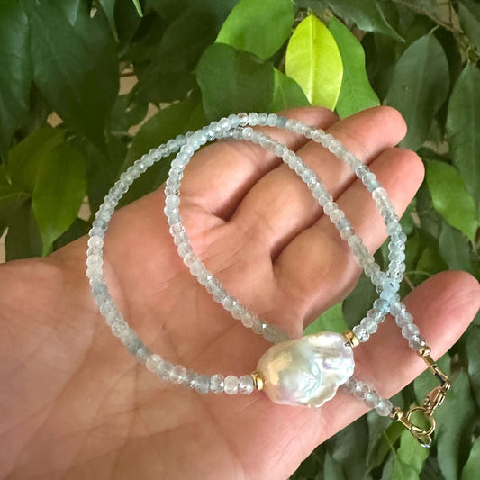 Aquamarine pearl necklace held in hand against green leaves