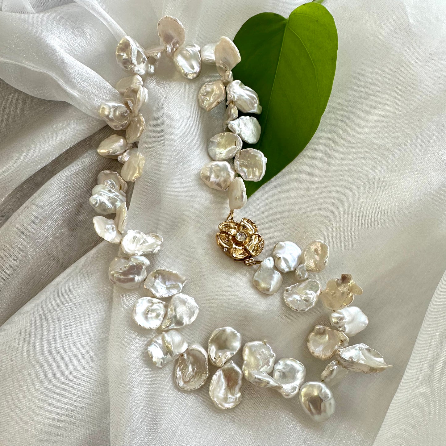 Close-up of white keshi pearl necklace with flower clasp on white fabric showing iridescent luster