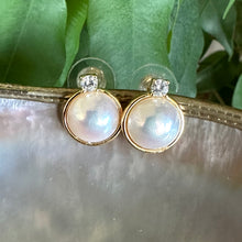 Load image into Gallery viewer, Close-up of Mabe Edison pearl stud earrings with cubic zirconia halo on shell and leaf background