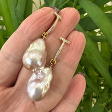 Load image into Gallery viewer, Pink baroque pearl hoop earrings held in hand against green foliage, designed and handmade in Canada.