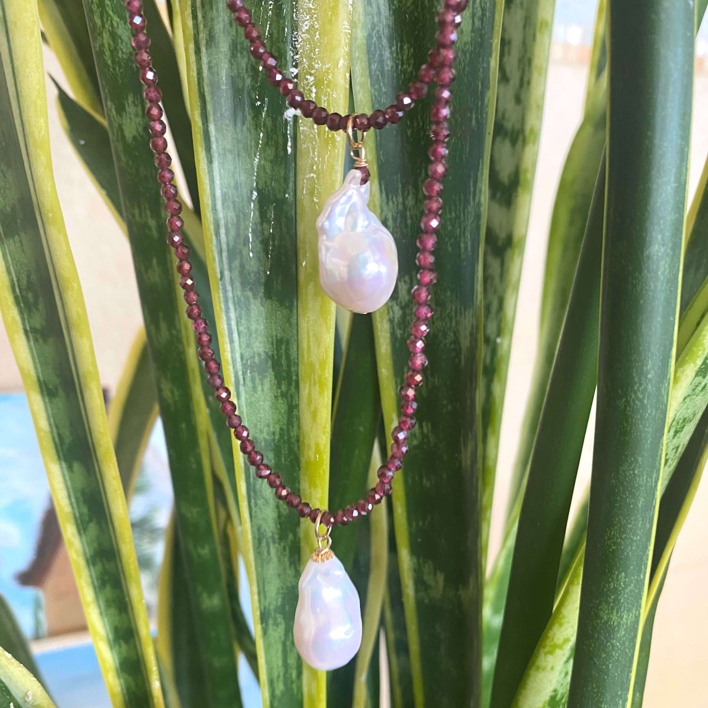 Red garnet baroque pearl necklace with vibrant garnet beads and a luminous Baroque pearl pendant on display.