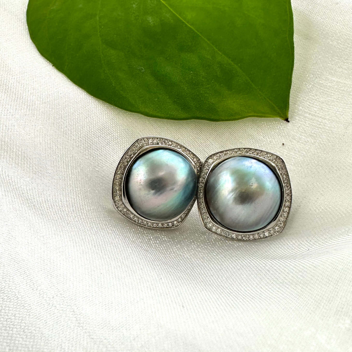 Mabe Pearl Earrings – shown on white cloth with green leaf accent