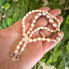 Load image into Gallery viewer, Handcrafted Rice Pearl Necklace with pastel pearls held in hand against green leaf background.