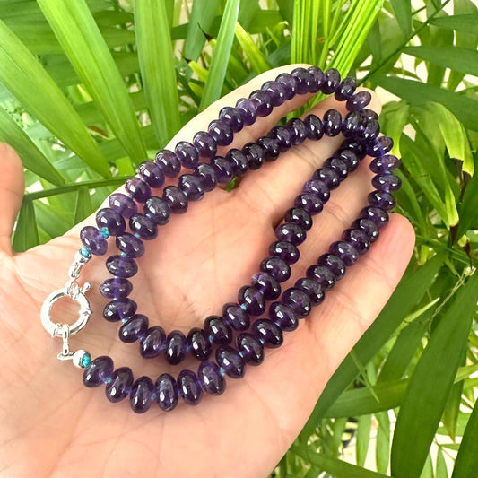 Close-up of handmade amethyst beaded necklace in dark purple tones against green leaf background