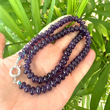 Load image into Gallery viewer, Close-up of handmade amethyst beaded necklace in dark purple tones against green leaf background