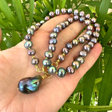 Load image into Gallery viewer, Black pearl pendant necklace held in hand for scale against green leaf background