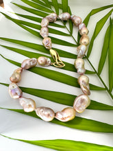 Load image into Gallery viewer, Close view of golden pink baroque pearl necklace against green leaf backdrop