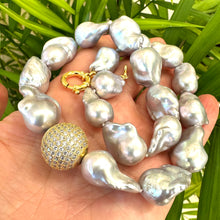 Load image into Gallery viewer, Silver grey baroque pearl necklace held in hand against green leaf background