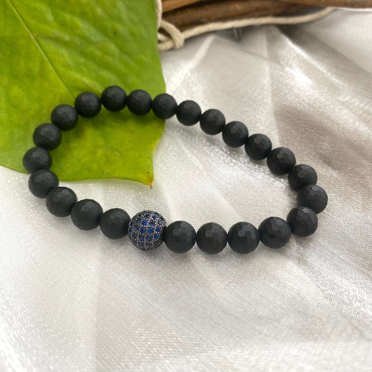 Matte black onyx mens bracelet featuring blue CZ centerpiece on a textured surface.