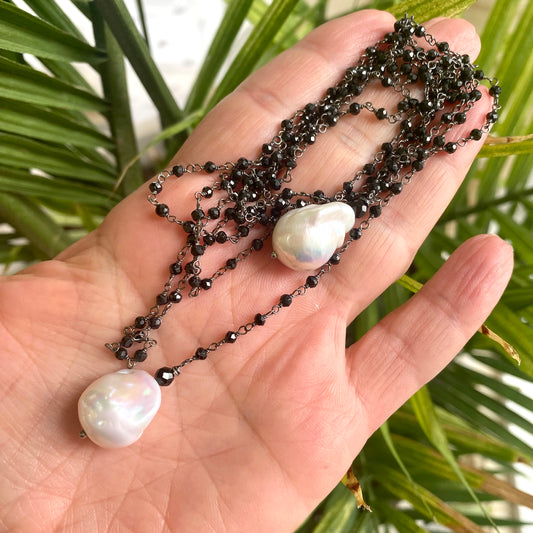 Black spinel lariat necklace held in hand against green foliage background showing natural shine
