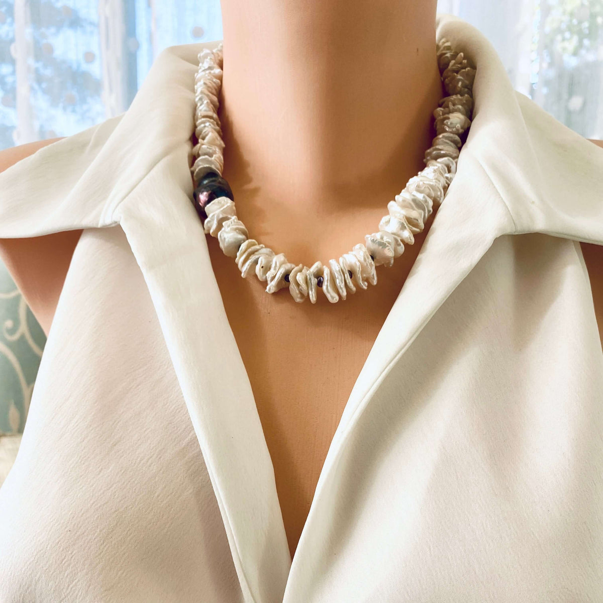 White cornflake pearl necklace with black baroque pearl pendant styled on a mannequin against a light background.