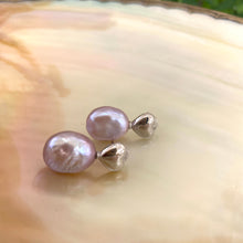 Load image into Gallery viewer, Heart Pearl Earrings – silver close-up against white pearl shell backdrop