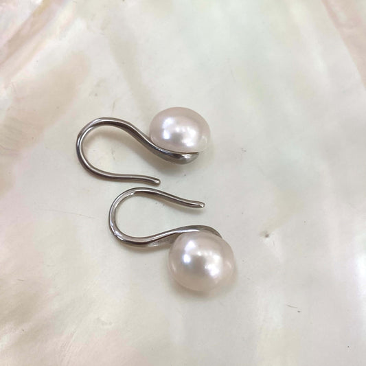 Button Pearl Earrings – silver version close-up against white pearl shell background
