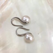 Load image into Gallery viewer, Button Pearl Earrings – silver version close-up against white pearl shell background