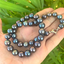 Load image into Gallery viewer, Black pearl necklace held in hand for scale against green leaf background