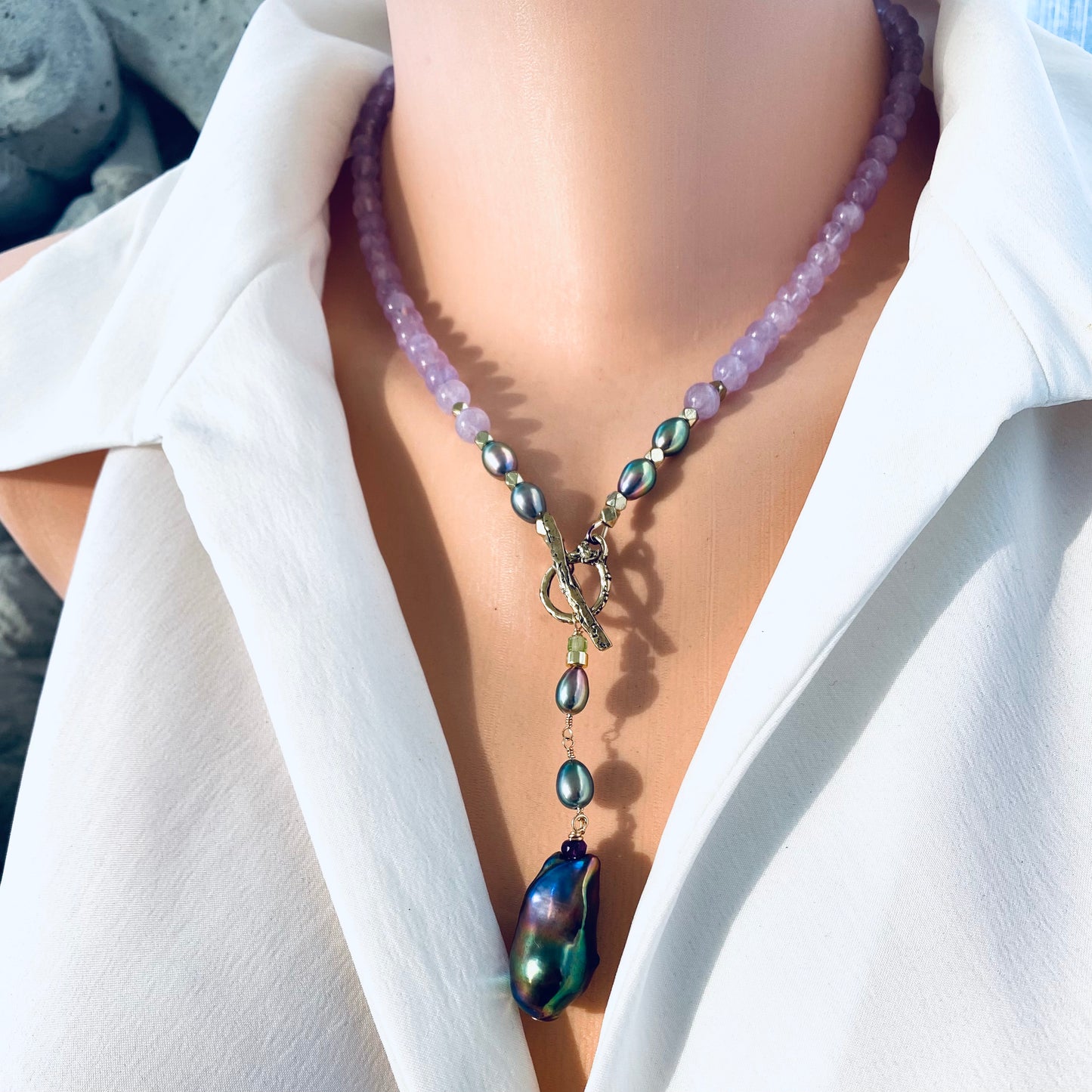 Close-up of Amethyst Pearl Necklace showing lavender amethyst gems and peacock black baroque pendant on mannequin.