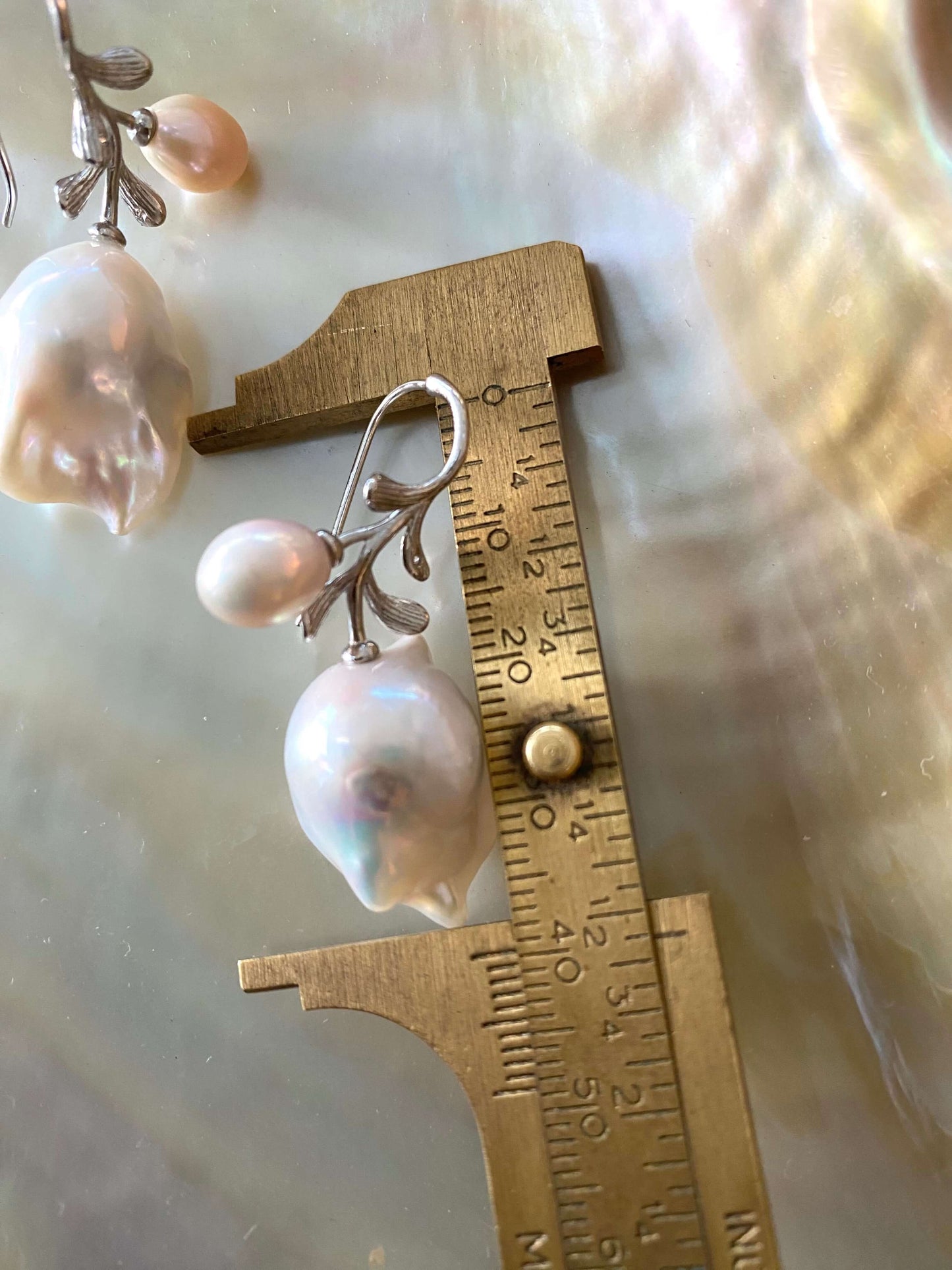 Close-up of baroque pearl earrings in silver measured with ruler on white backdrop