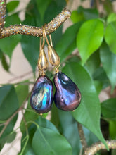 Load image into Gallery viewer, Baroque pearl drop earrings in black peacock hues held in hand against green leaf background