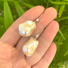 Load image into Gallery viewer, Golden Baroque Pearl Earrings – held by hand against green leaf backdrop