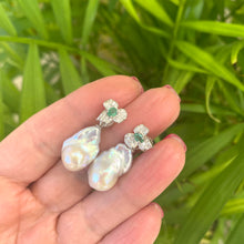 Load image into Gallery viewer, Emerald stud earrings with pearl drops held in hand against green leaf backdrop