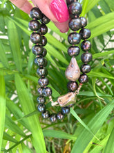 Load image into Gallery viewer, Close view of black pearl necklace with rose gold pendant against green leaf backdrop