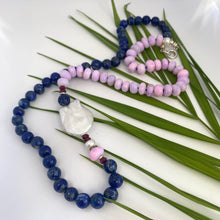 Load image into Gallery viewer, Close-up of lapis lazuli and baroque pearl necklace with ruby detail on white and leaf background.