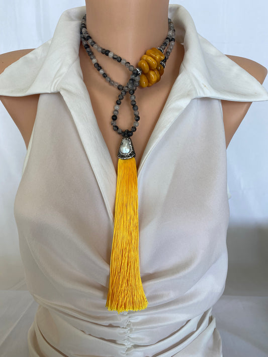 Boho rutilated quartz necklace with yellow copal tassel on mannequin, frontal medium shot.