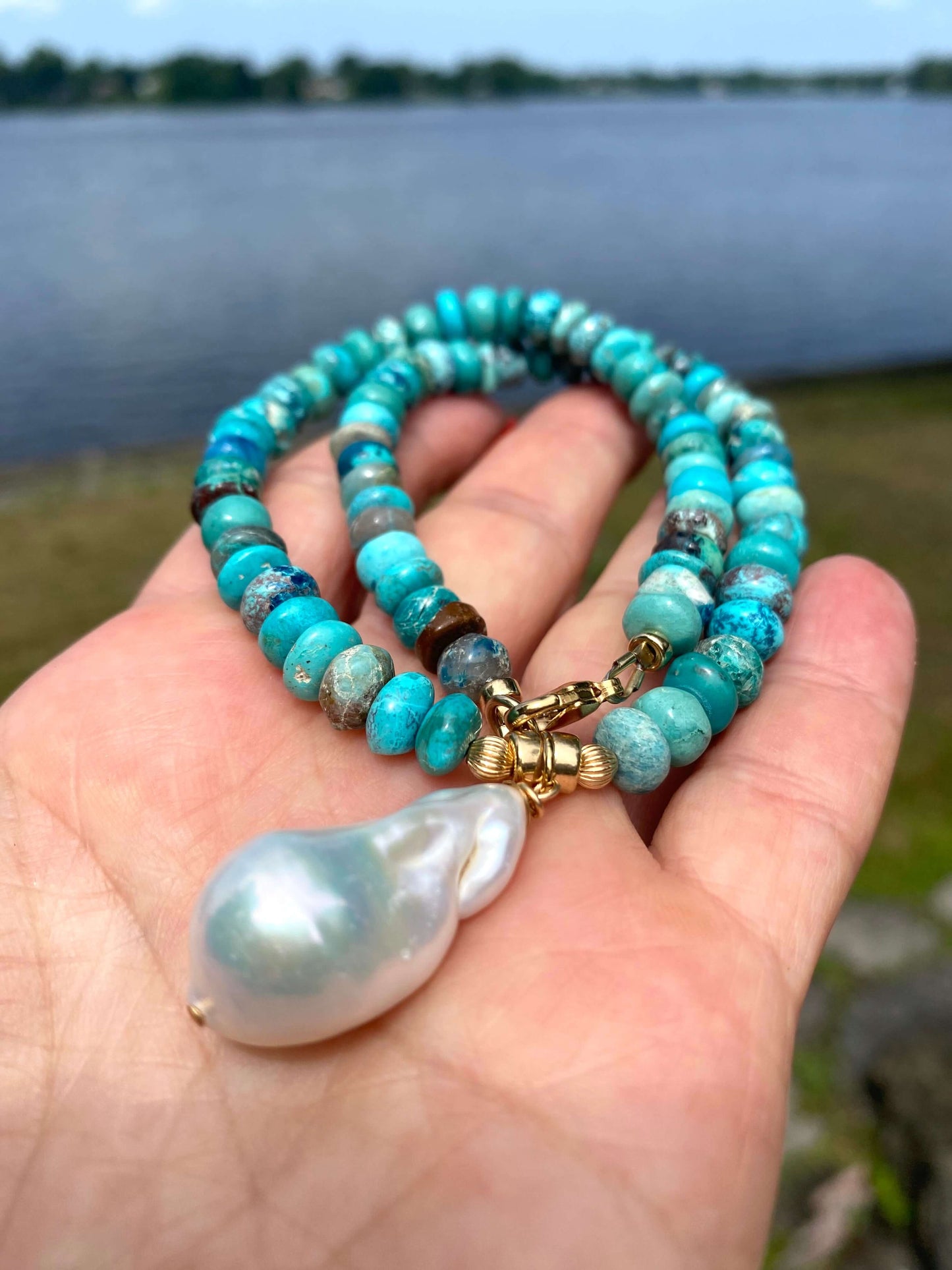 Turquoise pearl necklace featuring Arizona turquoise beads and a baroque pearl pendant, showcased on a hand near water.