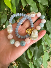 Lade das Bild in den Galerie-Viewer, Blue jade morganite aquamarine pearl necklace showcasing baroque gem design, held in hand among lush foliage.