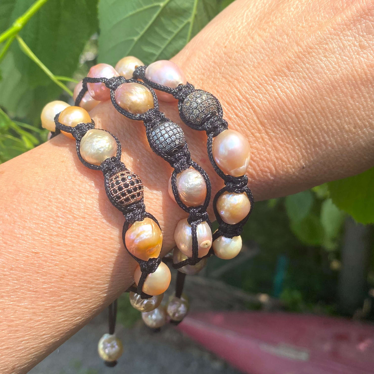 Baroque pearl bracelet featuring pastel pearls and black thread, elegantly wrapped around a wrist in a natural setting.