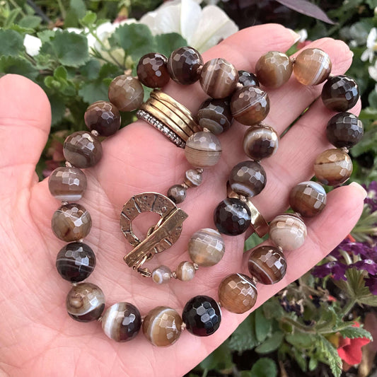 Botswana agate candy necklace with gold bronze details showcased in a hand among colorful flowers.
