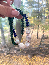 Load image into Gallery viewer, Malachite Lapis Lazuli Baroque Pearl Necklace held in hand against green leaf backdrop, designed and handmade in Canada.