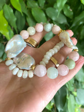 Lade das Bild in den Galerie-Viewer, Hand holding morganite and jade necklace with baroque pearls against green natural foliage, showing gemstone color and luster.