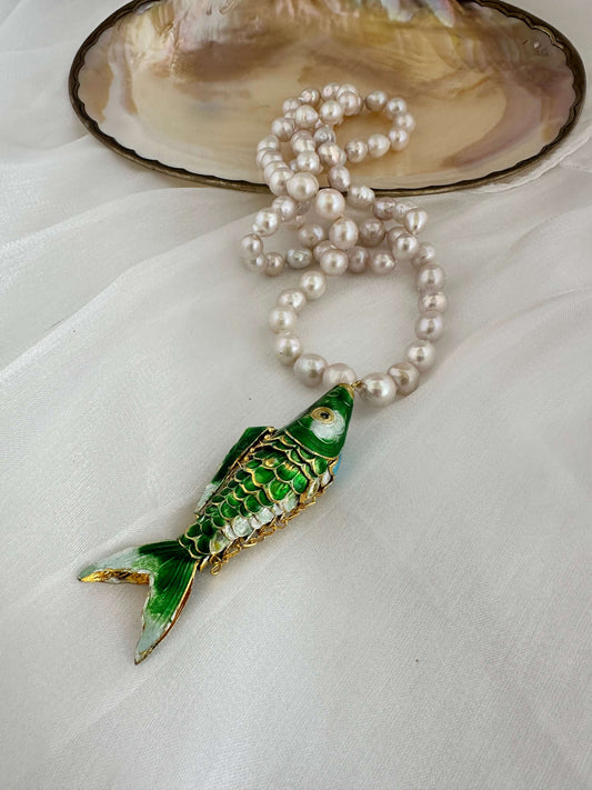 Cloisonné fish pearl necklace featuring green fish pendant and hand knotted baroque pearls on soft fabric background