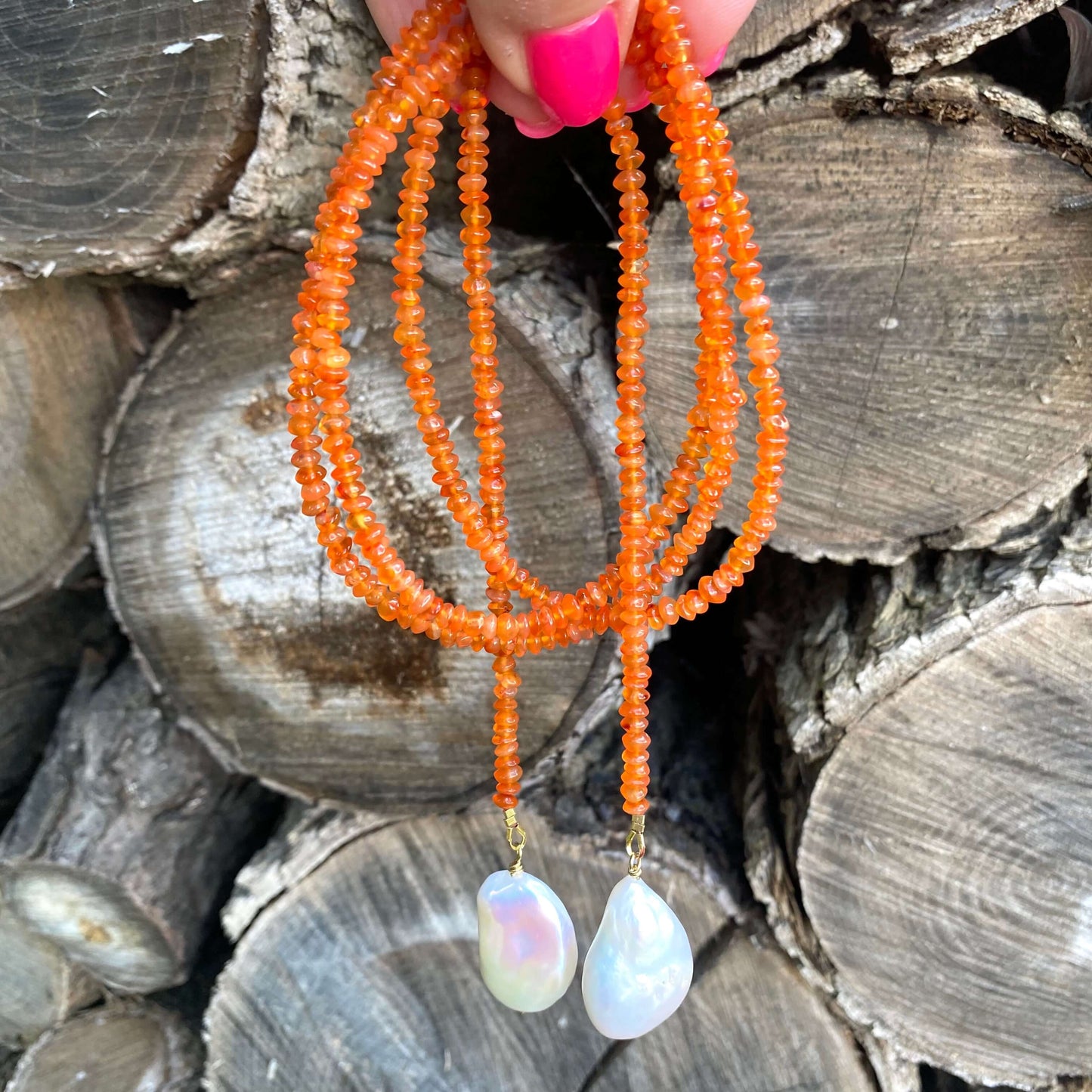 Close-up of a carnelian lariat necklace showcasing bright orange beads and two baroque pearls.