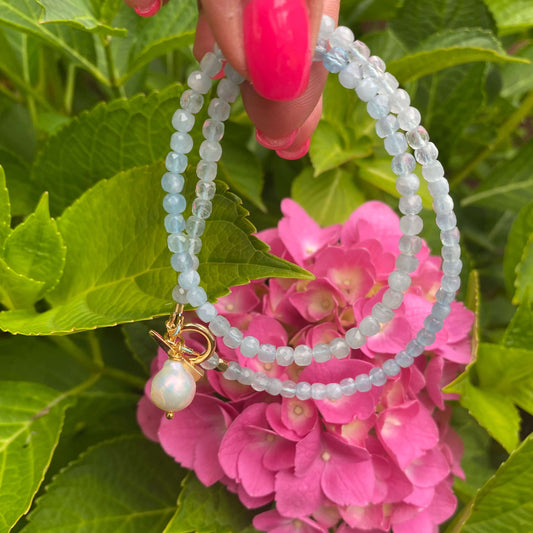 Aquamarine toggle necklace with baroque pearl pendant displayed against pink hydrangeas.