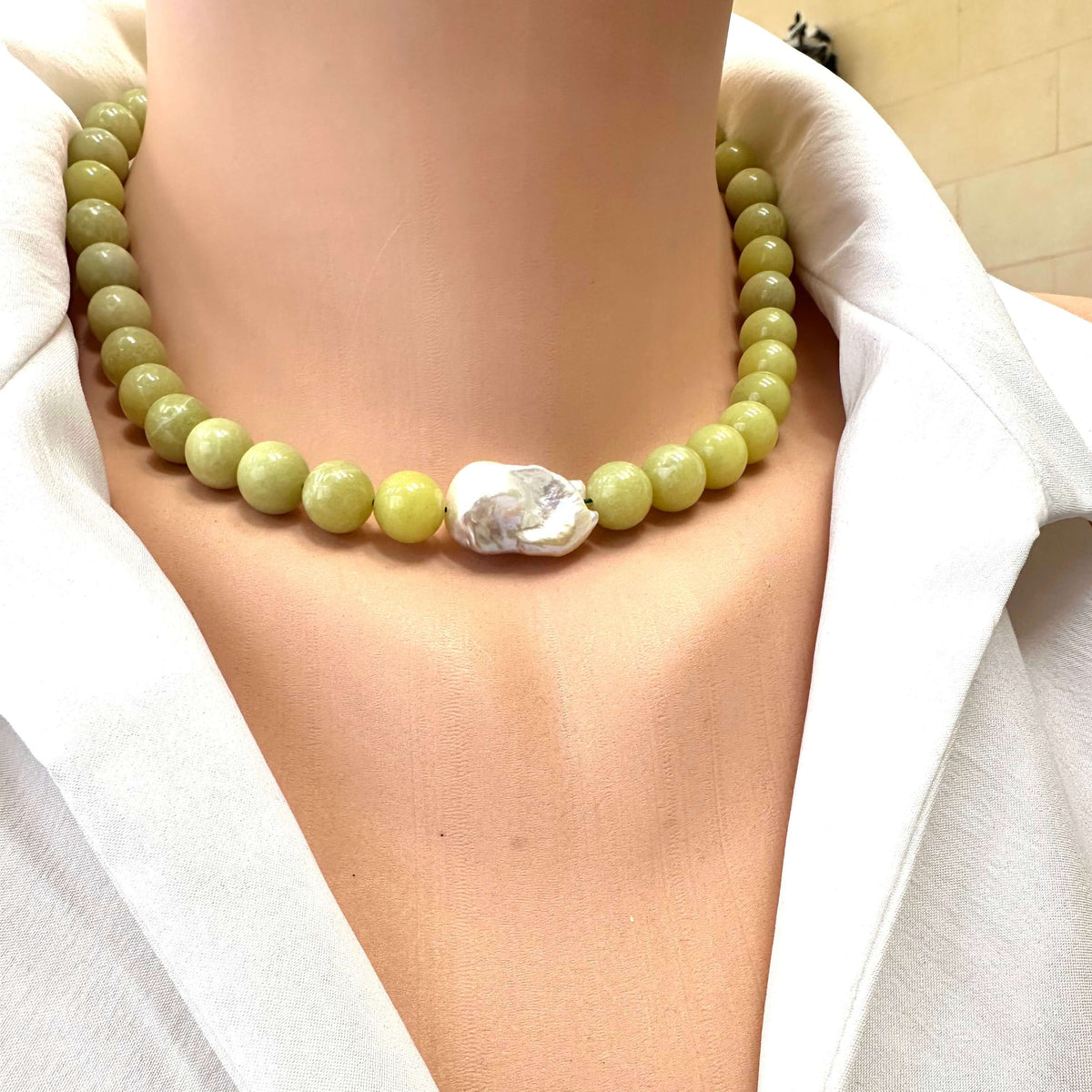 Necklace with green beads and a large white stone worn by a person in a white outfit.